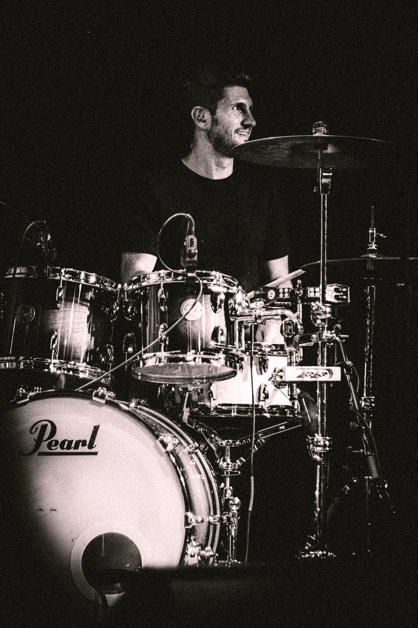 Smiling drummer playing a Pearl drum set under spotlight on a dark stage. bandkaroke.live