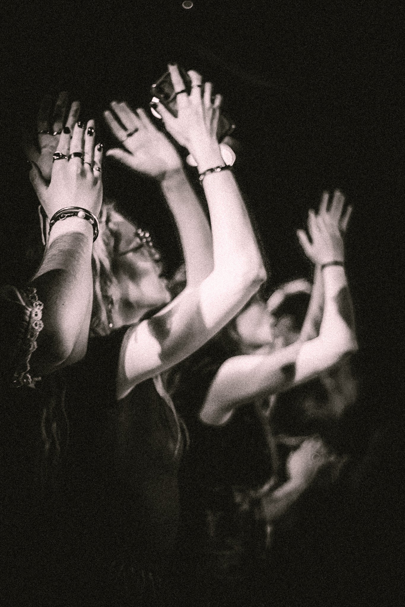 People raising their hands enthusiastically in a dimly lit concert or event setting. bandkaroke.live