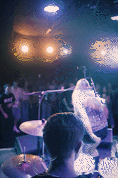 Live music performance with drummer in foreground, vocalist in background, and bright stage lights. bandkaroke.live