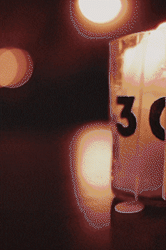 Close-up of a candle holder with the number 30, glowing softly against a dark background with bokeh lights. bandkaroke.live