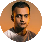 Portrait of a man with short dark hair and a serious expression, wearing a light-colored shirt against an orange background.