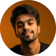 Portrait of a young man with short dark hair and a trimmed beard smiling slightly against an orange background.