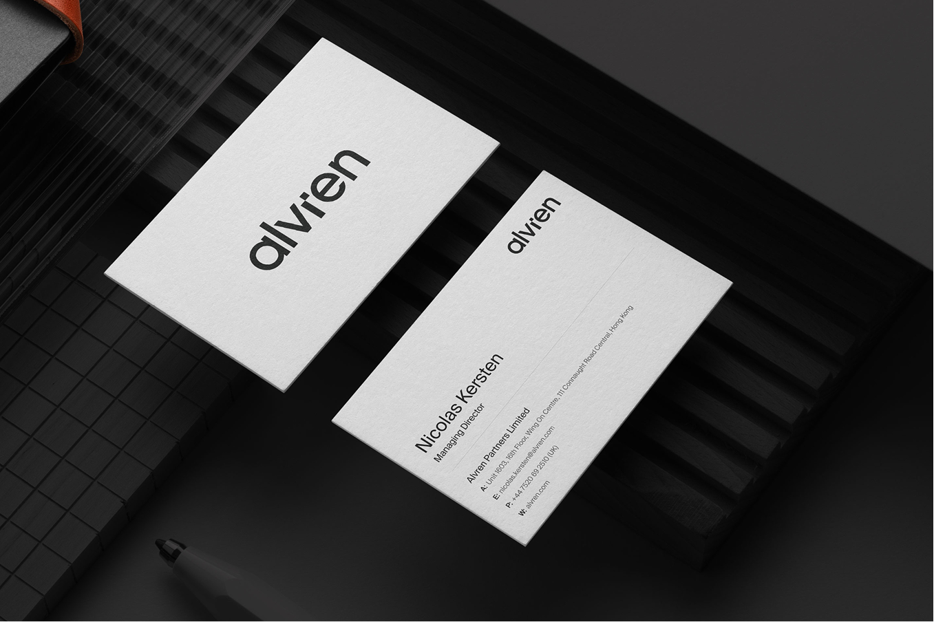 A top-down mockup of Alvren business cards on a dark, textured surface. One card shows the bold black Alvren logo on a white background, while the other displays professional contact details for "Nicolas Kersten, Managing Director" of Alvren Partners Limited. 