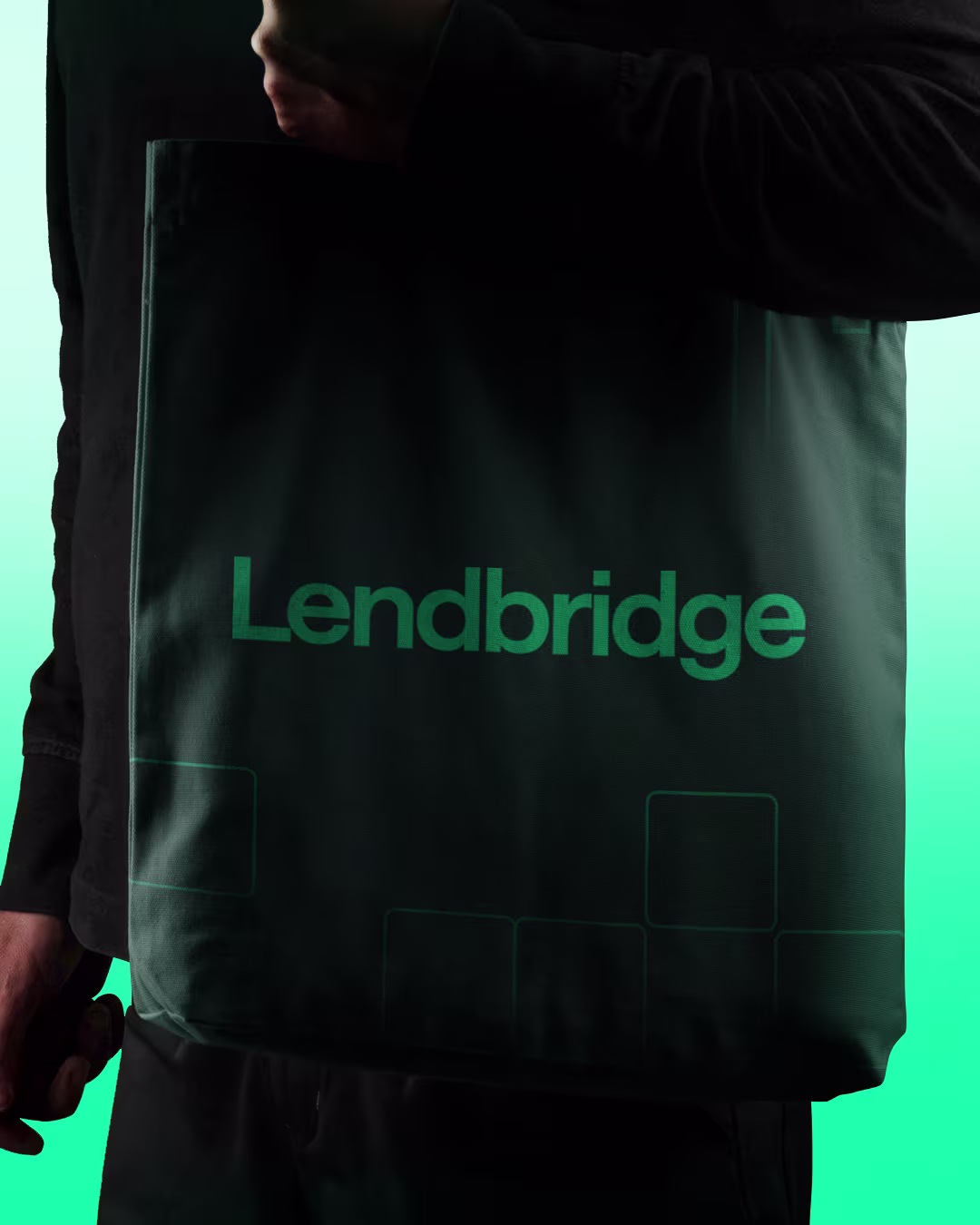 Close-up of a dark green tote bag featuring the Lendbridge wordmark in a bright green print with a subtle geometric square pattern at the bottom.