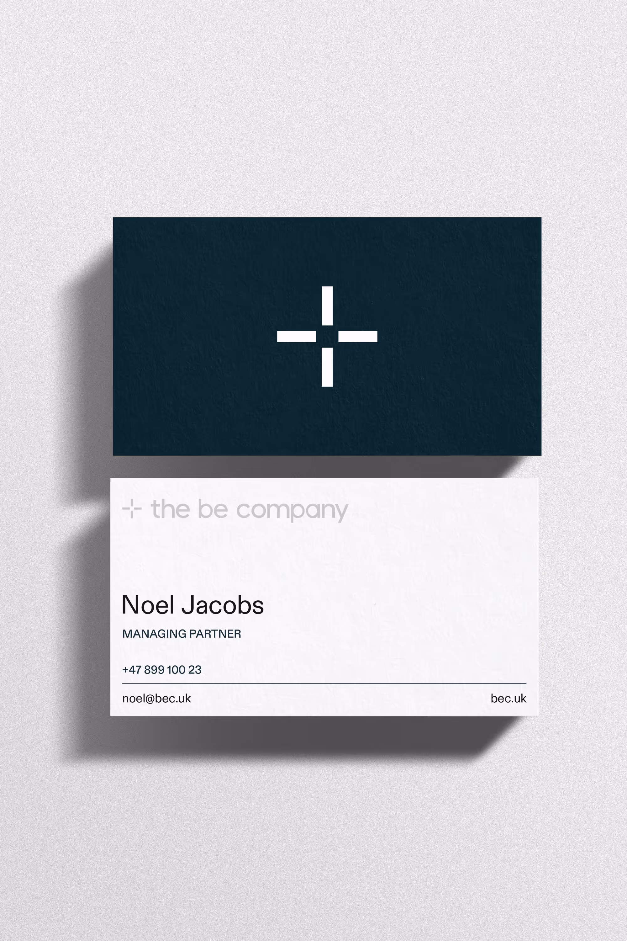 Minimalist business cards for The Be Company showing the dark green back with a white plus logo and the white front for Managing Partner Noel Jacobs. 