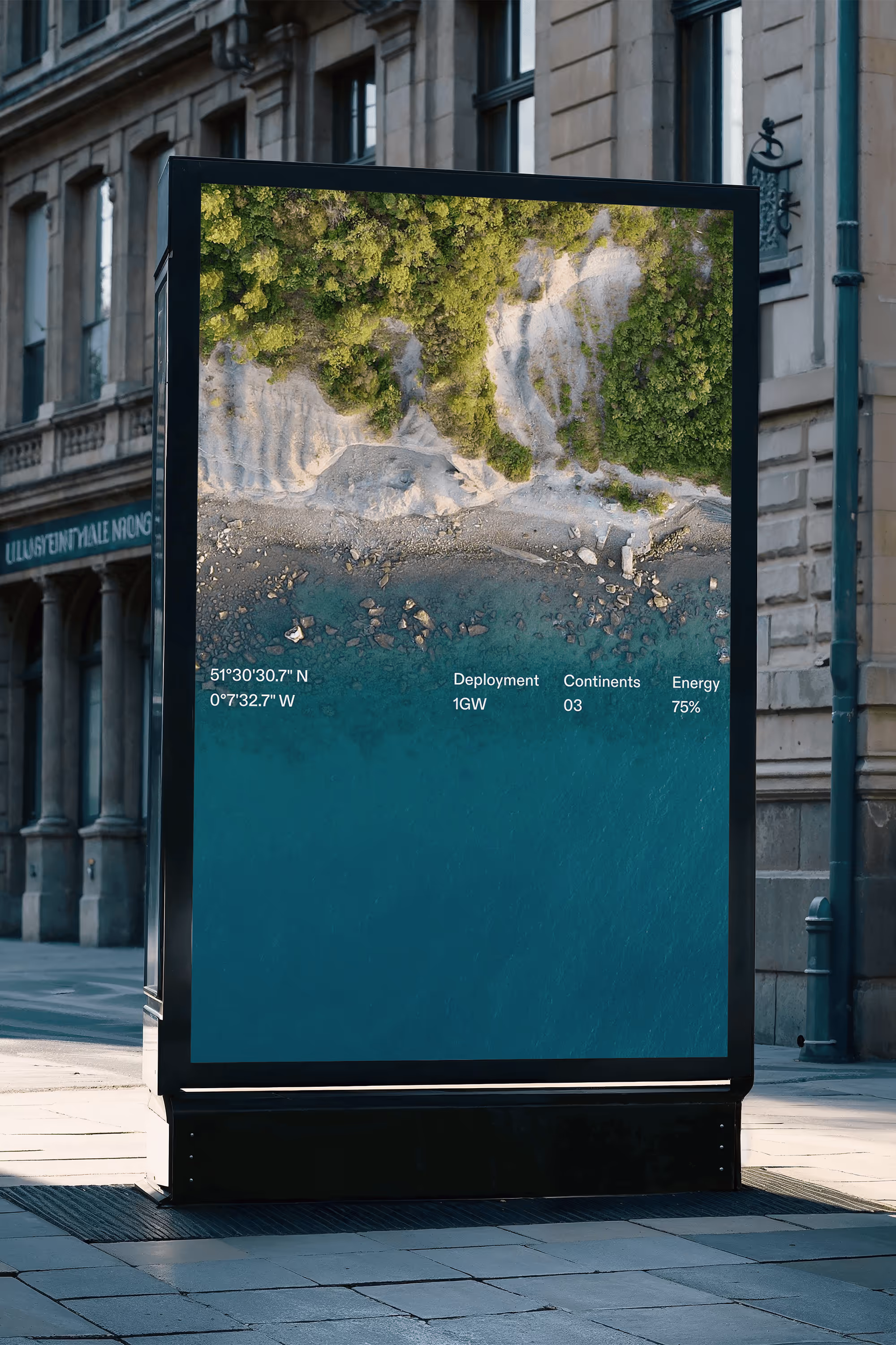 A large vertical digital billboard on a city sidewalk displaying an aerial coastal image with The Be Company’s deployment data overlay.