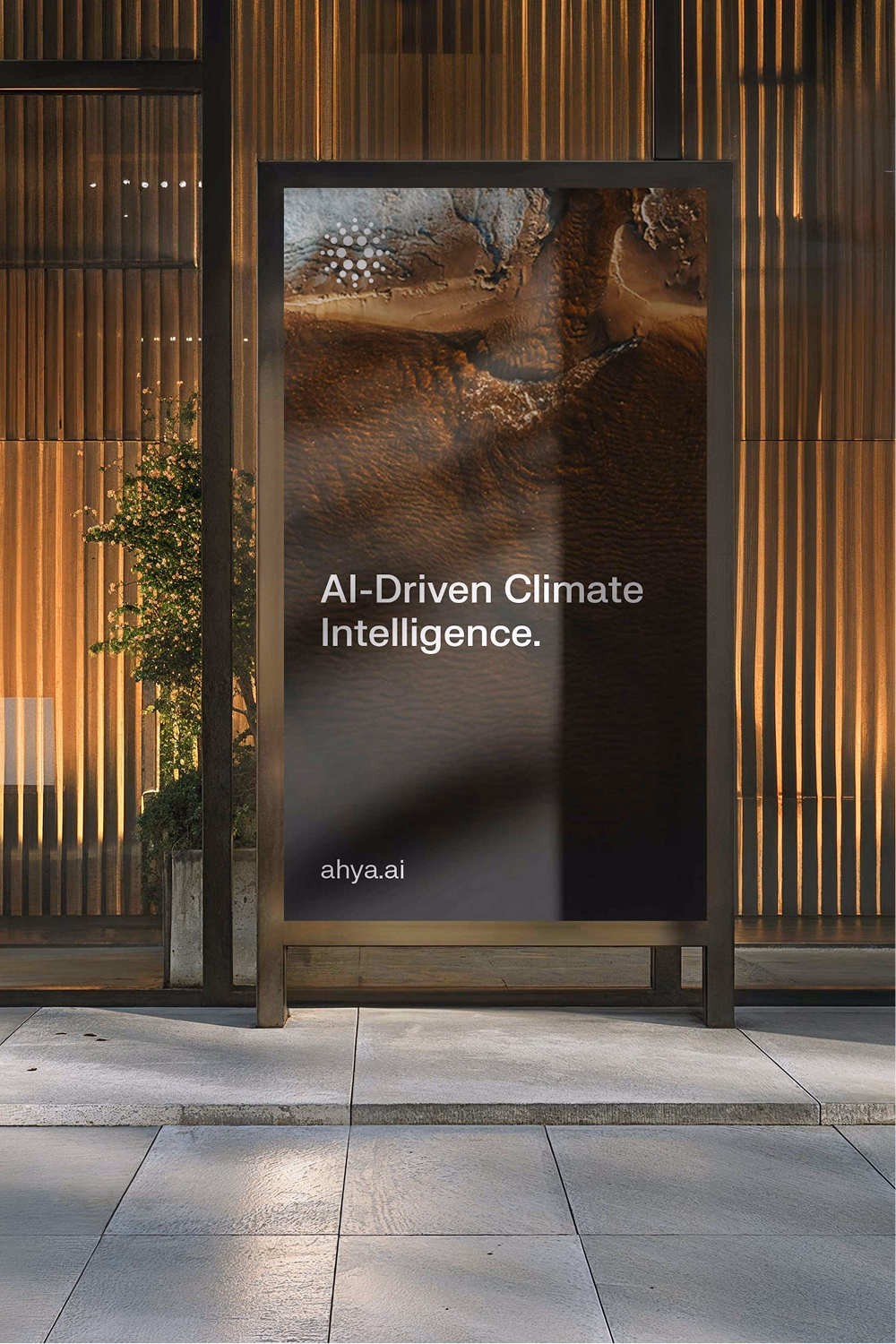 A vertical digital billboard in a modern urban setting. The display shows a satellite-style view of earth in warm brown tones with the text "AI-Driven Climate Intelligence" and the URL "ahya.ai." 