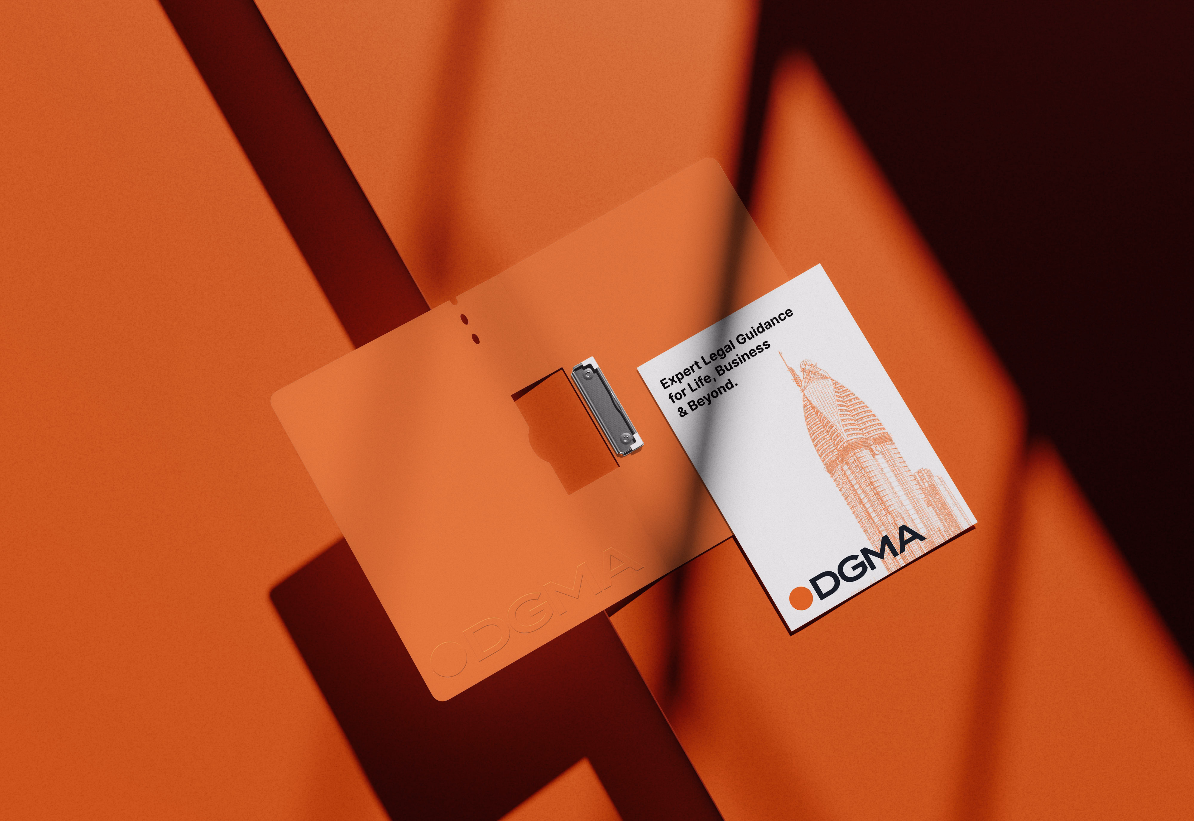 A brand stationery mockup for DGMA, featuring an embossed orange folder and a white business card with a skyscraper illustration and the tagline "Expert Legal Guidance for Life, Business & Beyond."