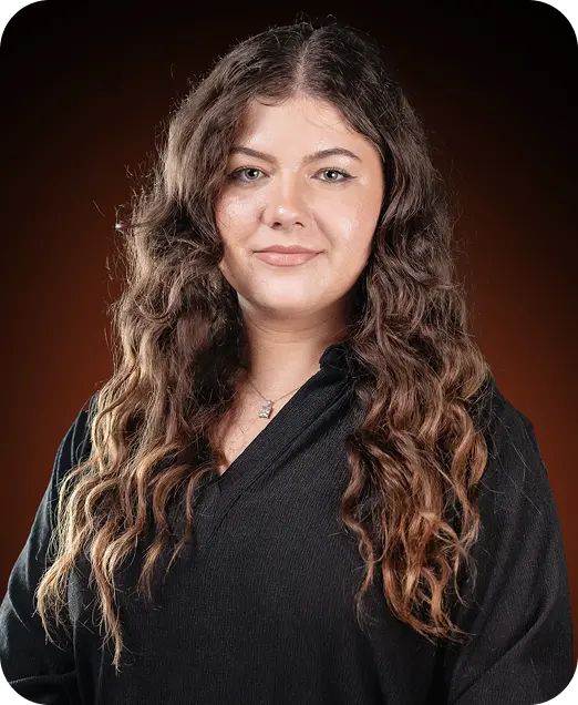 A woman with long, wavy hair wearing a black top against a dark background.