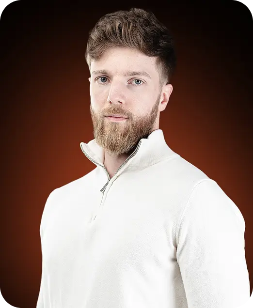 Portrait of a young man with brown hair and a beard wearing a white quarter-zip sweater against a dark brown background.