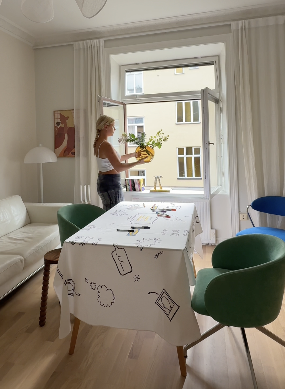 Creator setting a communal dining table with the IKEA LÅNGDUK tablecloth inside a bright modern apartment.