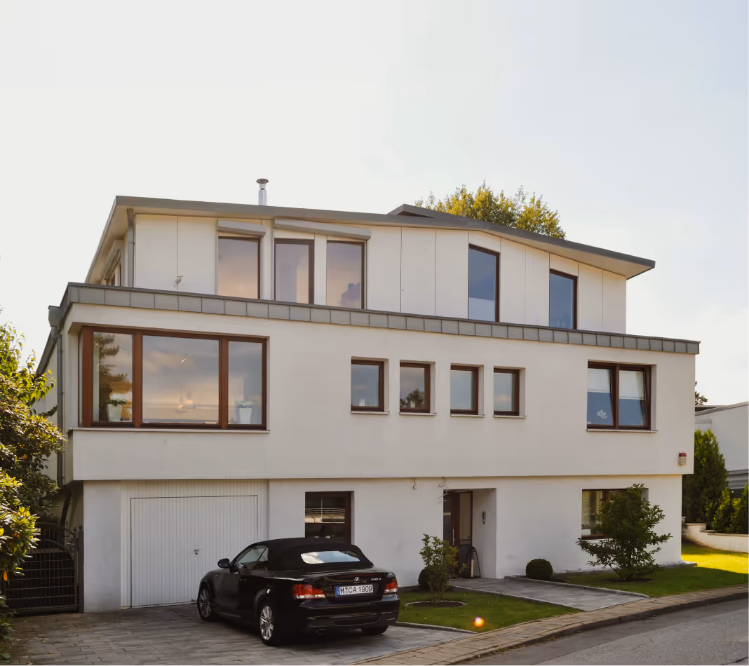 Modern mehrstöckiges Haus mit weißen Wänden, großen Fenstern und schwarzem Cabrio auf der Einfahrt.