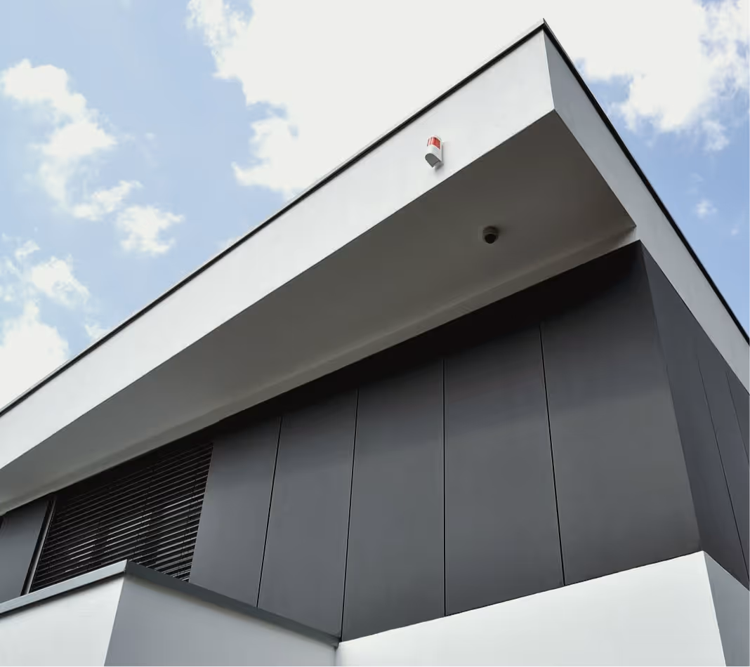Ansicht der modernen Gebäudeecke mit weißem Dach und dunkler Fassade unter blauem Himmel.