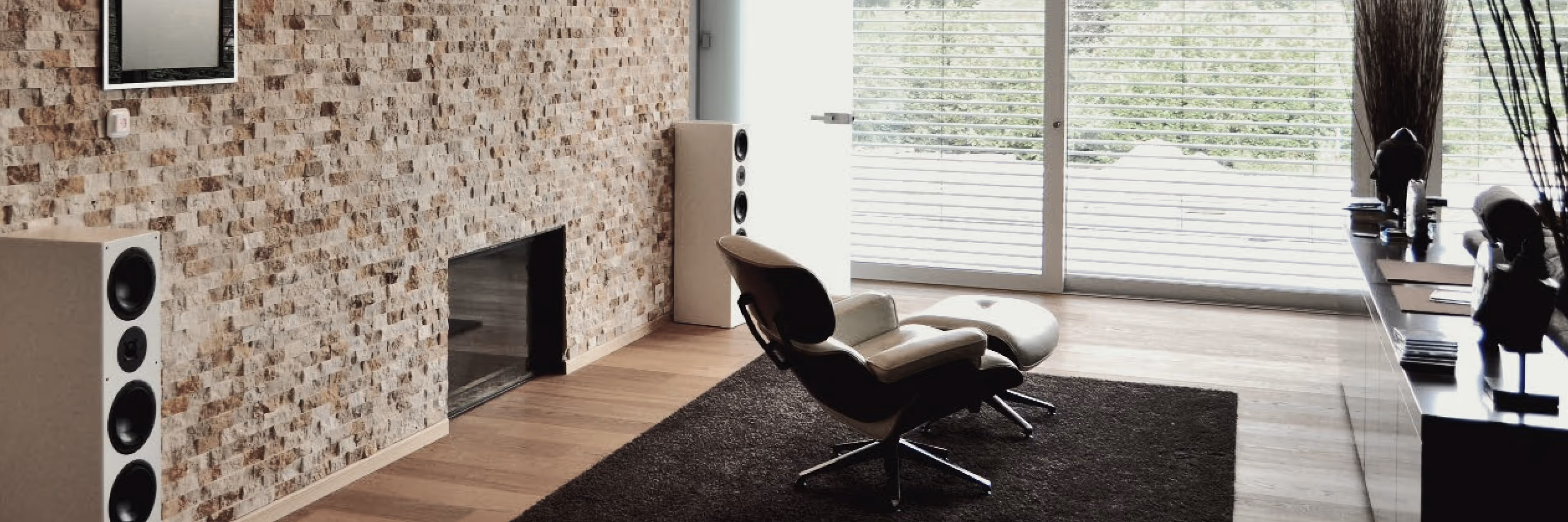 Modern Wohnzimmer mit Steinwand, Ledersessel, Hocker und großem Fenster mit Jalousien.