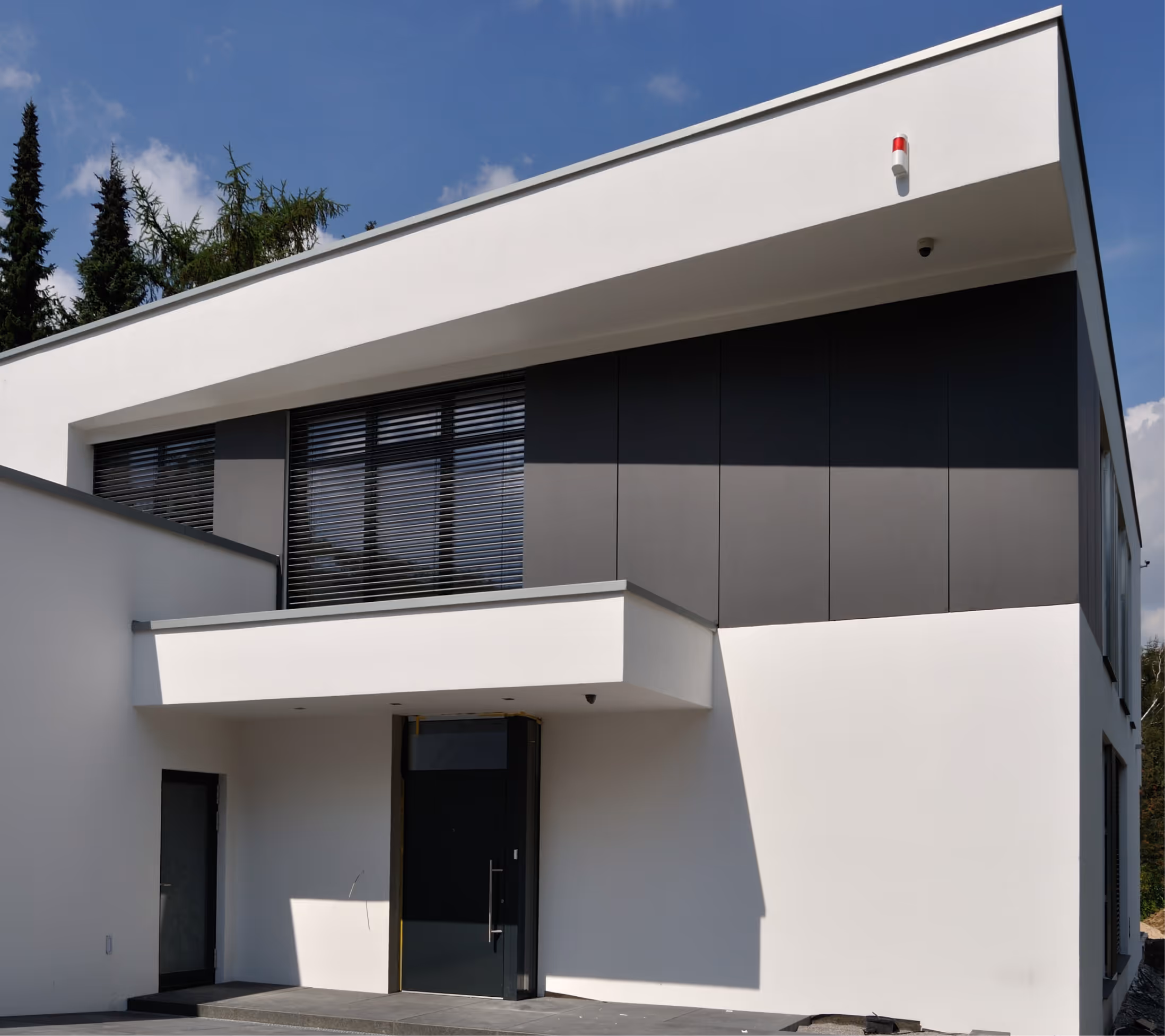 Modern weißes Haus mit dunklen Fensterläden und einem überdachten Eingang bei sonnigem Himmel.