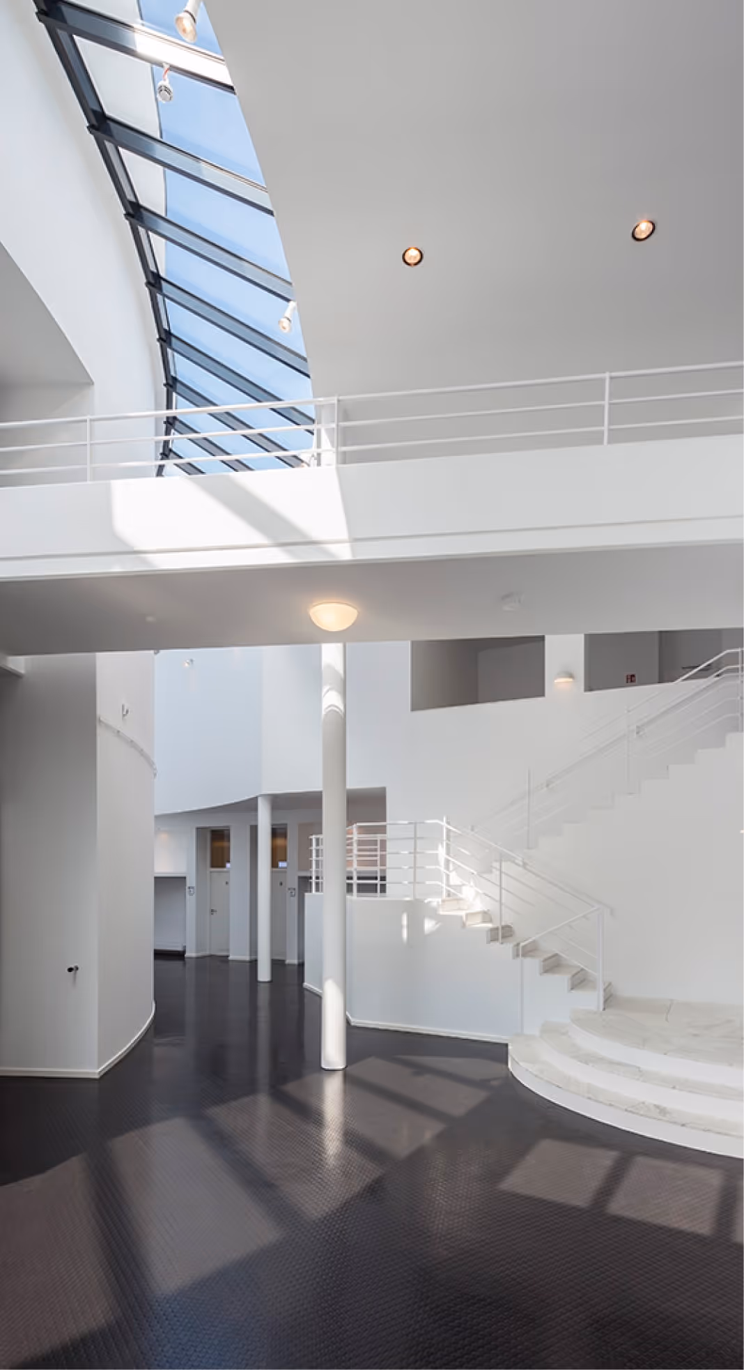 Heller Innenraum mit weißen Wänden, Treppen, Säulen und großem Glasdach, das Licht hereinlässt.