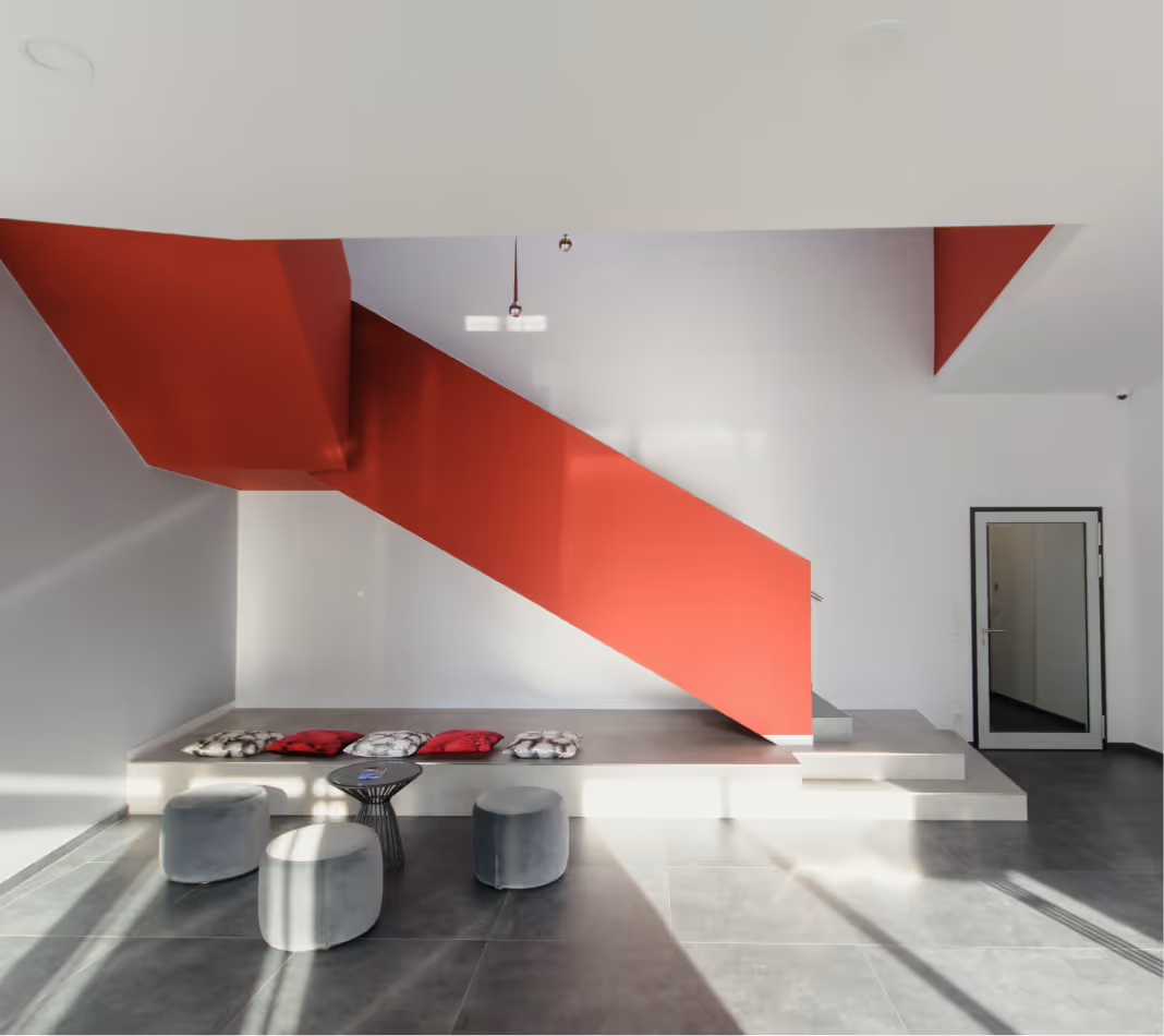 Modern interior with red staircase, gray poufs, and cushions on gray tiled floor.