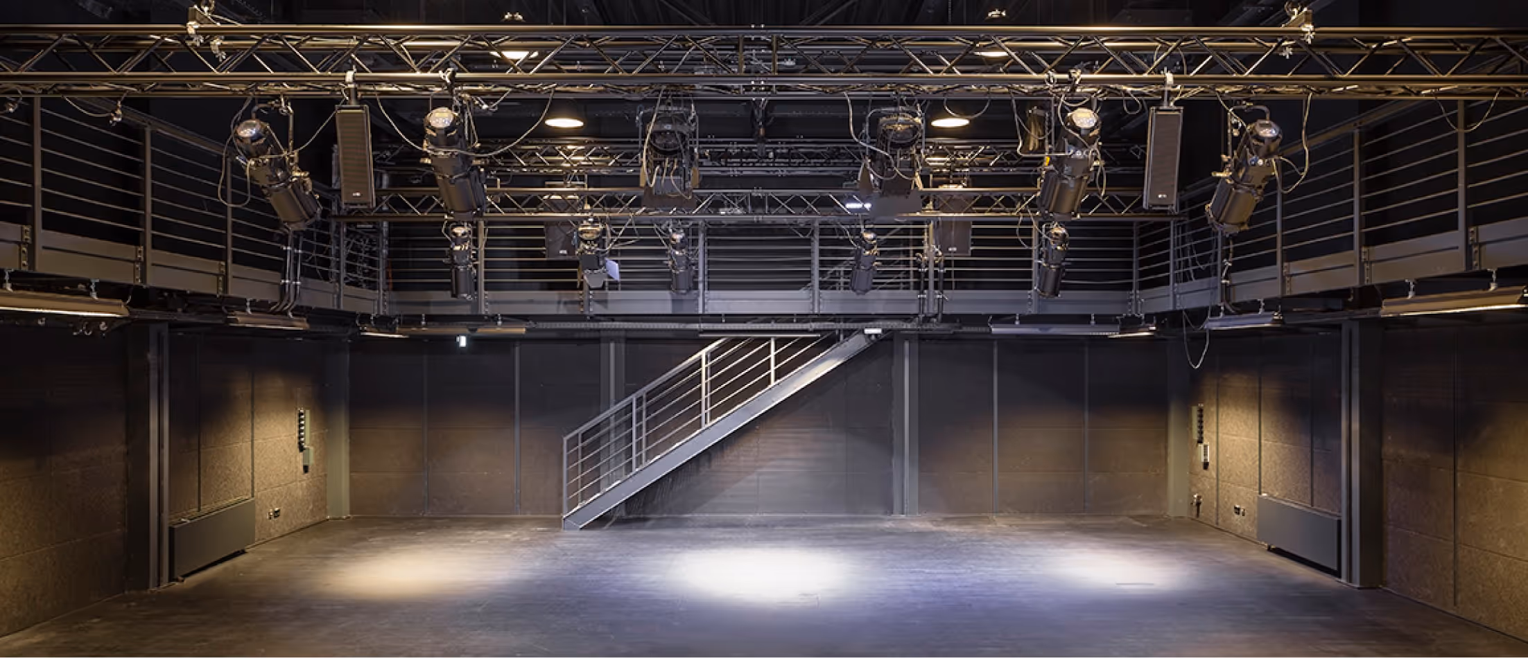 Leerer schwarzer Veranstaltungsraum mit Beleuchtungstechnik und Metalltreppe an der Rückwand.