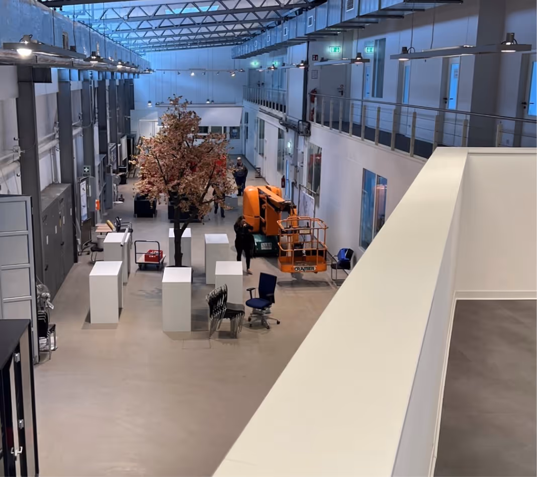 Großer moderner Raum mit weißen Säulen, künstlichem Baum und orangener Hebebühne.