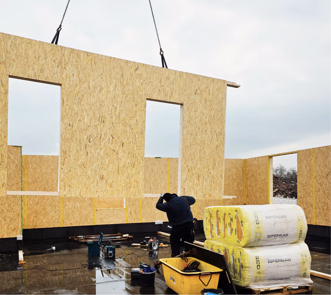 Bauarbeiter beim Aufrichten von vorgefertigten Holzplattenwänden auf einer Baustelle.