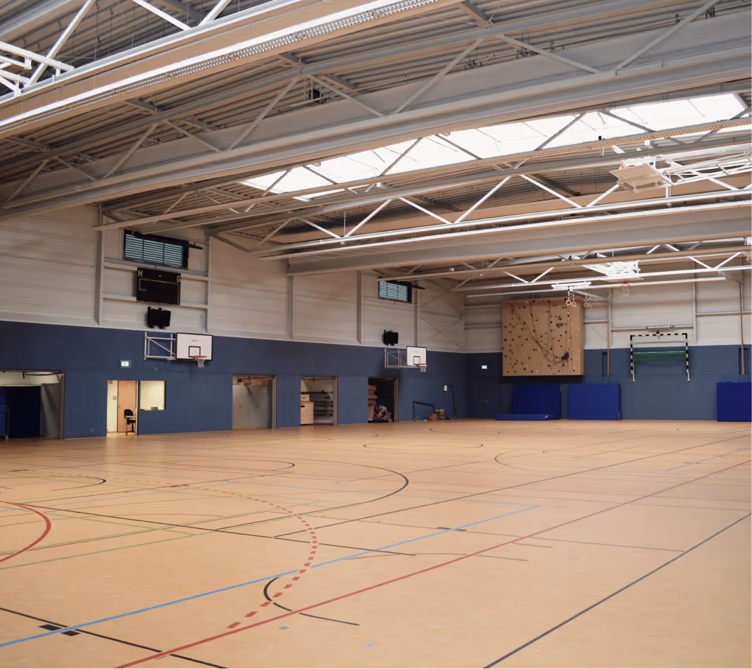Helle Mehrzweck-Sporthalle mit Spielfeldmarkierungen, Basketballkörben und Oberlichtern.