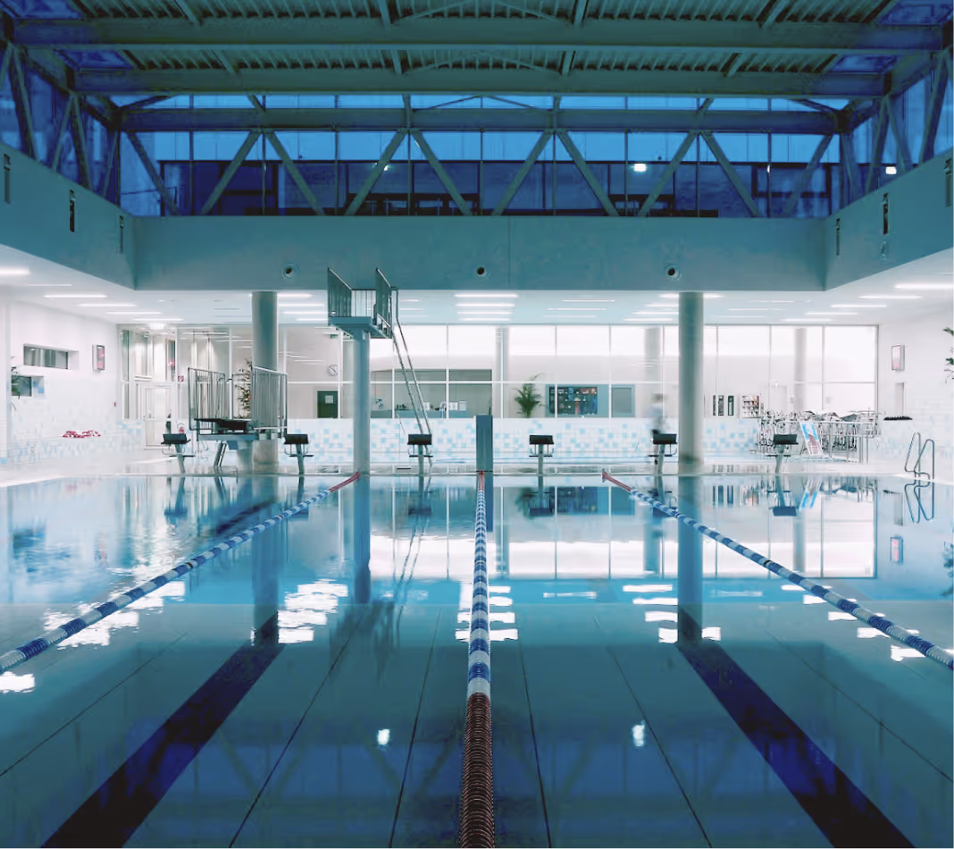 Hallenbad mit mehreren Schwimmbahnen, Sprungtürmen und weißen Wänden mit Fenstern.