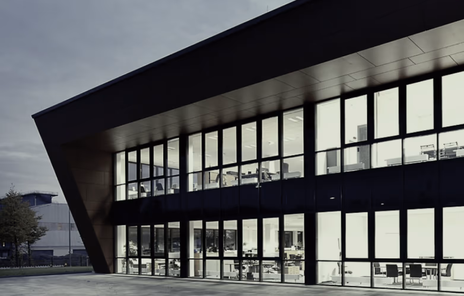 Modernes Bürogebäude mit großer Fensterfront und Innenansicht von Arbeitsplätzen bei Dämmerung.