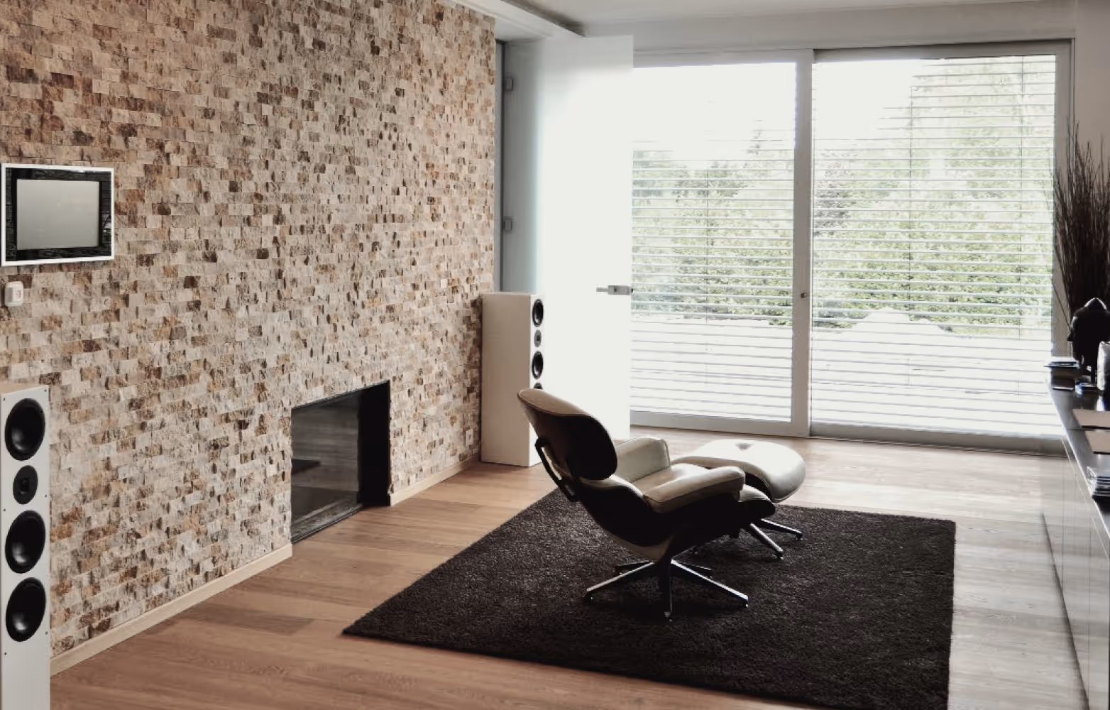 Moderner Wohnraum mit Ledersessel, passendem Hocker, braunem Teppich und Steinfasewand.