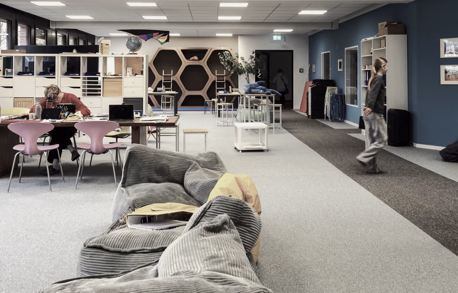Moderner Arbeitsbereich mit Sofas, Schreibtischen, Stühlen und offenen Regalen in hellem Raum.