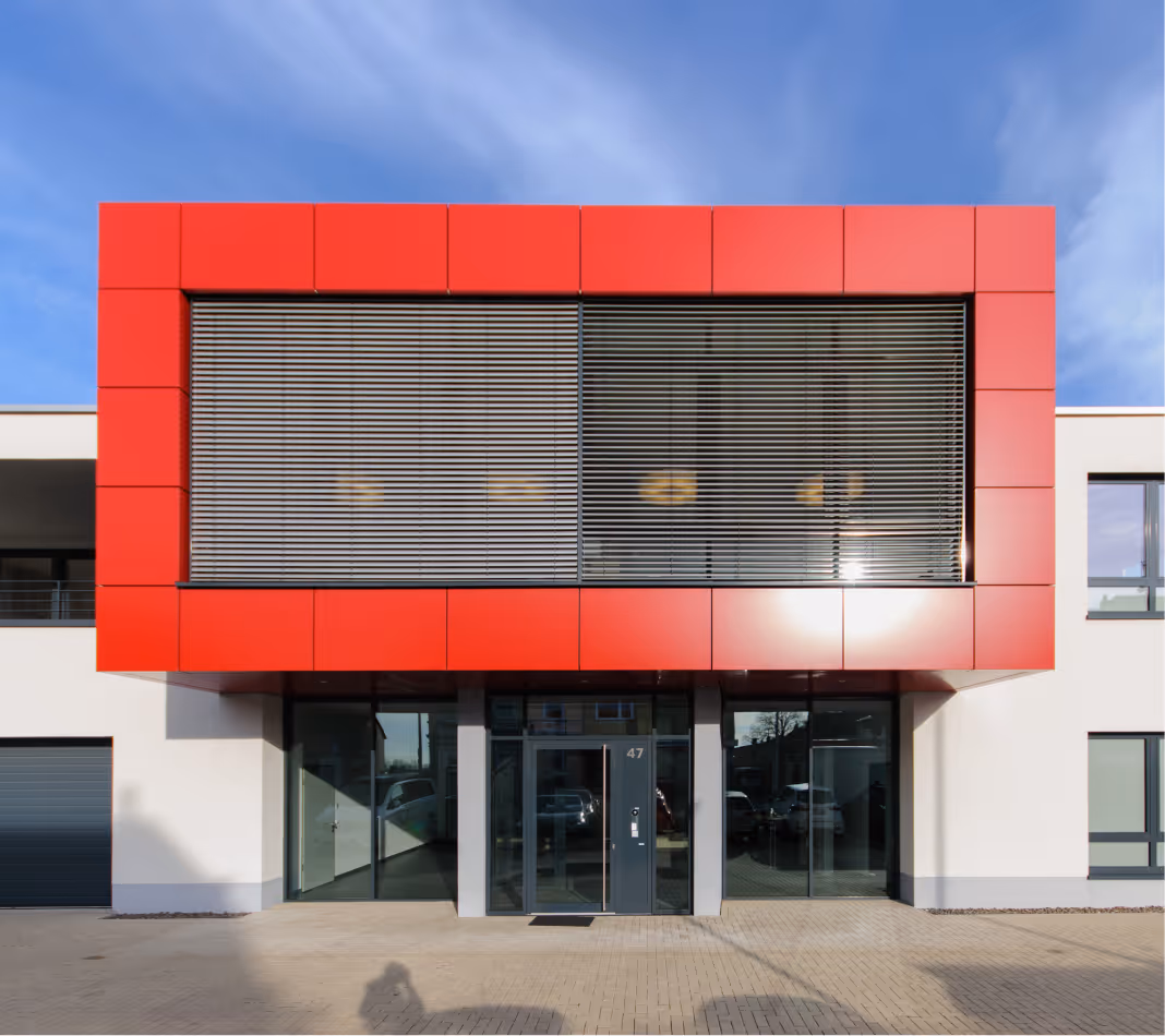 Modernes Gebäude mit rotem Rahmen und großen Fenstern unter blauem Himmel.