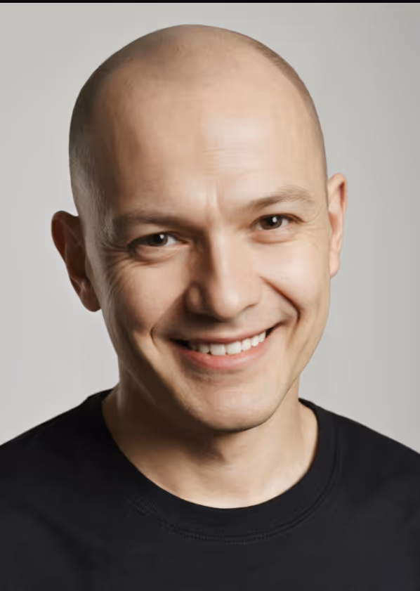 Smiling bald man wearing a black crew neck shirt against a neutral background.