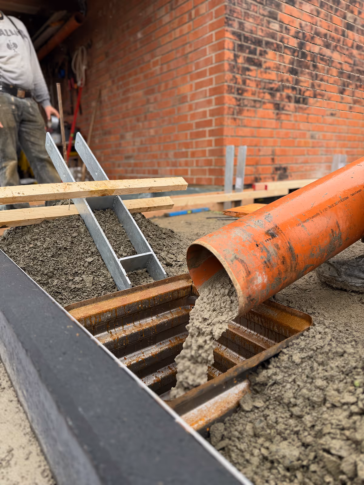 Beton wird über eine Schüttrinne in die Schalung an einer Backsteinwand gefüllt