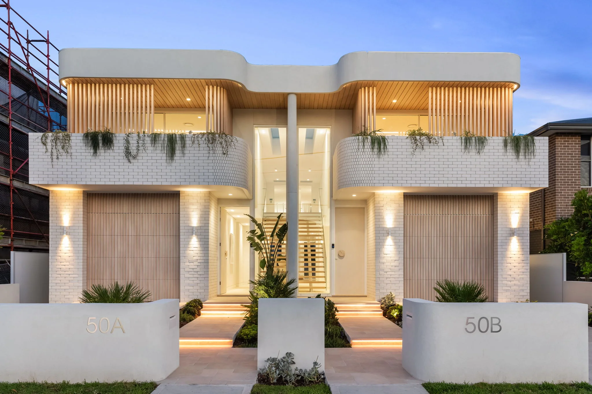 Modern duplex with white brick exterior, illuminated steps, and balconies with plants labeled 50A and 50B.