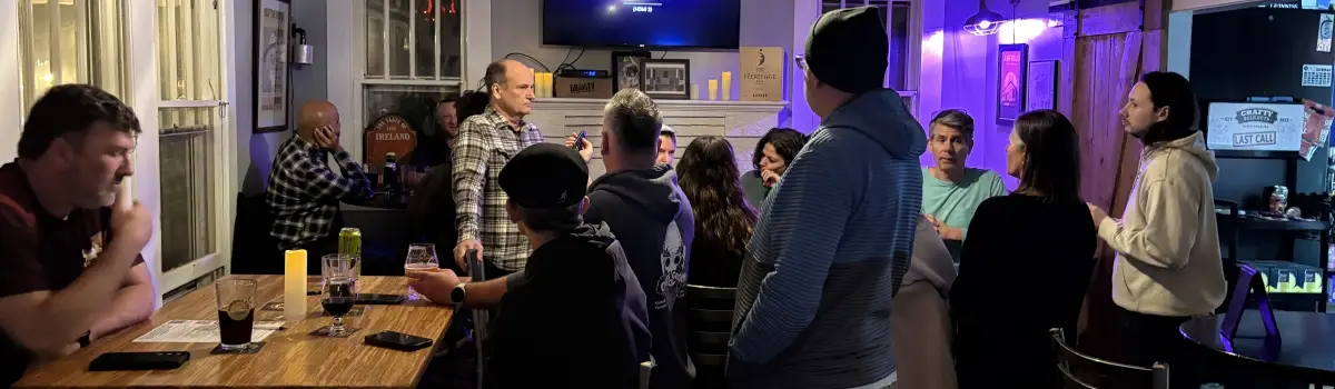 Crowd gathered around tables at Crafty Beer Guys bar during trivia night with TV screen and host leading the game