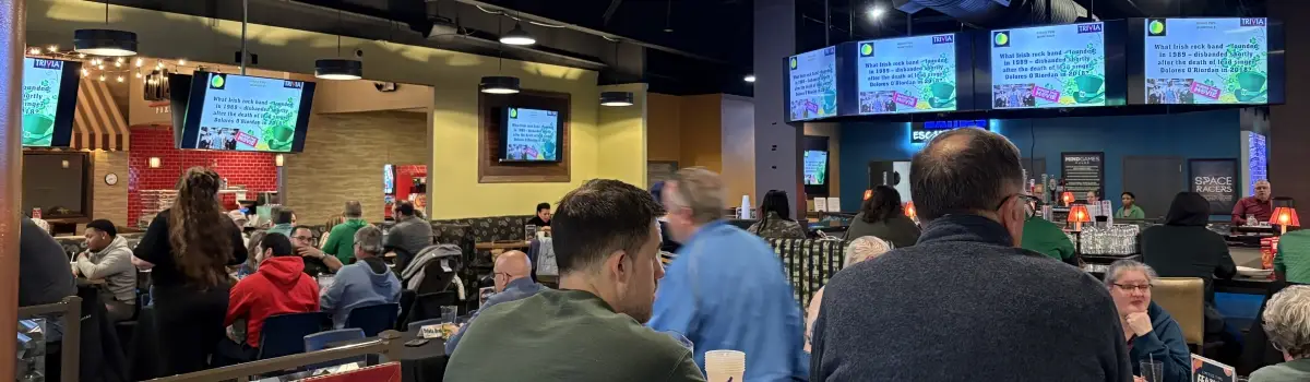 Crowd in Spare Time looking at TV screens with trivia questions on them