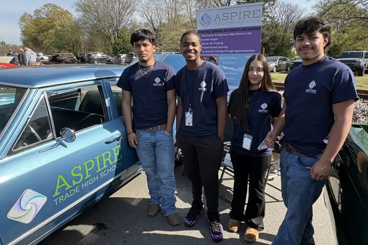 Four Aspire Trade High School students stand beside a car at a car show