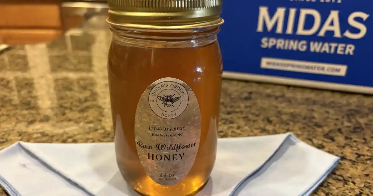 A 24 oz glass jar of Queen's Orders Honey brand raw wildflower honey