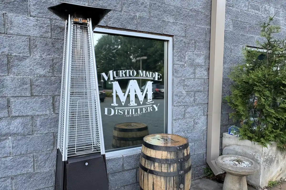 Murto Made Distillery window sign with outdoor barrels and patio heater