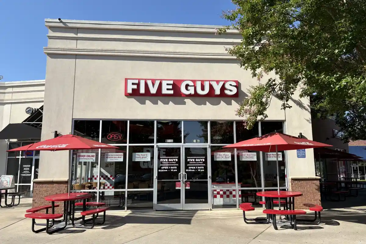 Entrance to Five Guys with outdoor tables next to the door to enter the restaurant