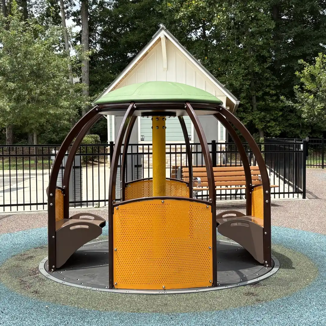 Modern merry-go-round with covered seating in the fenced playground at Rosedale Nature Park