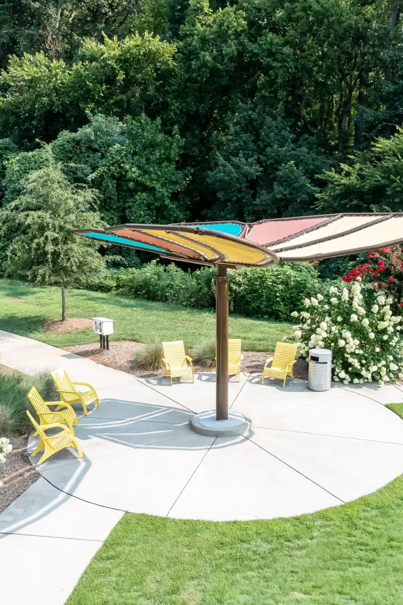 Butterfly-shaped shade structure with yellow Adirondack chairs on the walking oval at Rosedale Nature Park