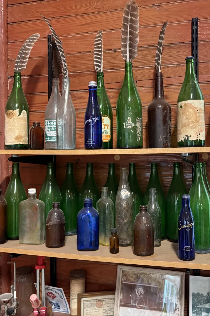 Display of antique glass bottles and feathers on a wood shelf