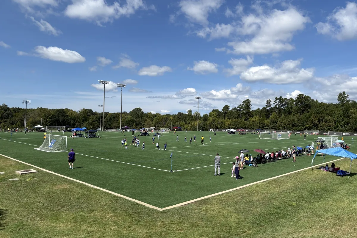 Soccer game underway on a synthetic turf field at Richard Barry Memorial Park with spectators along the sideline