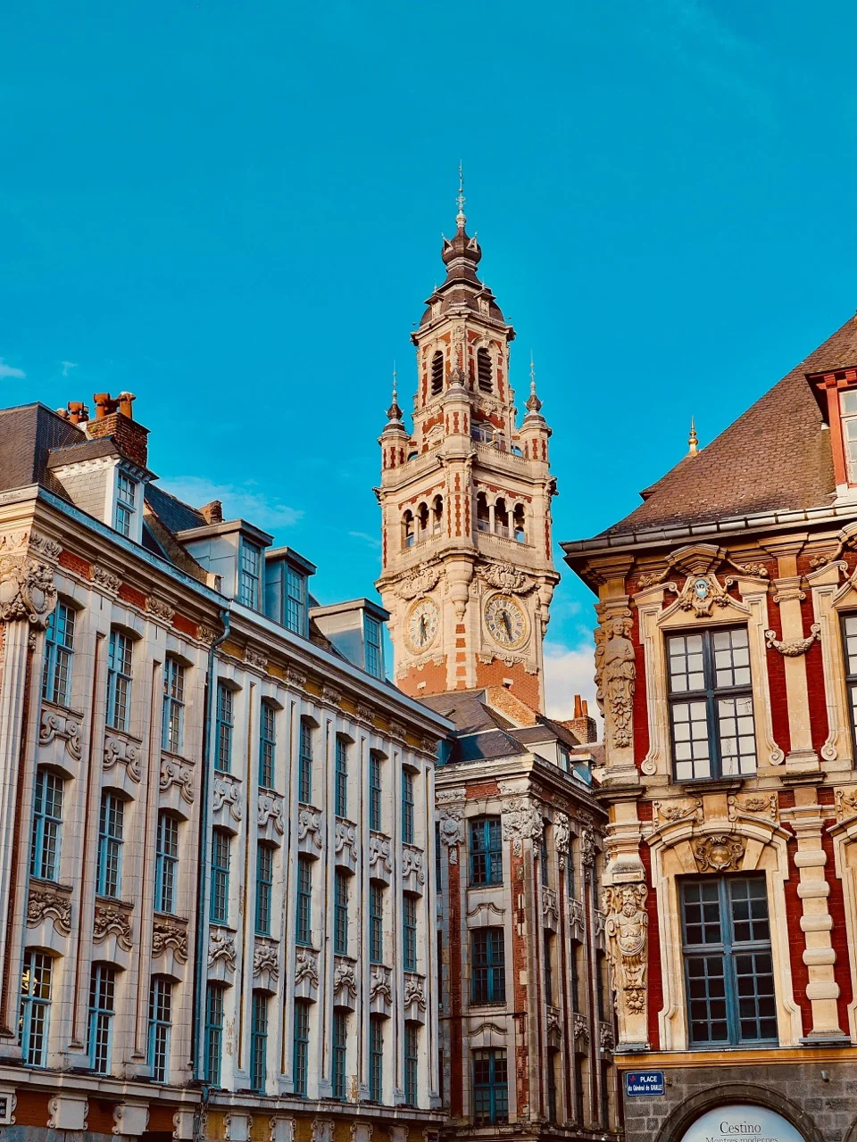 Façades historiques avec une tour d'horloge ornée sous un ciel bleu clair.