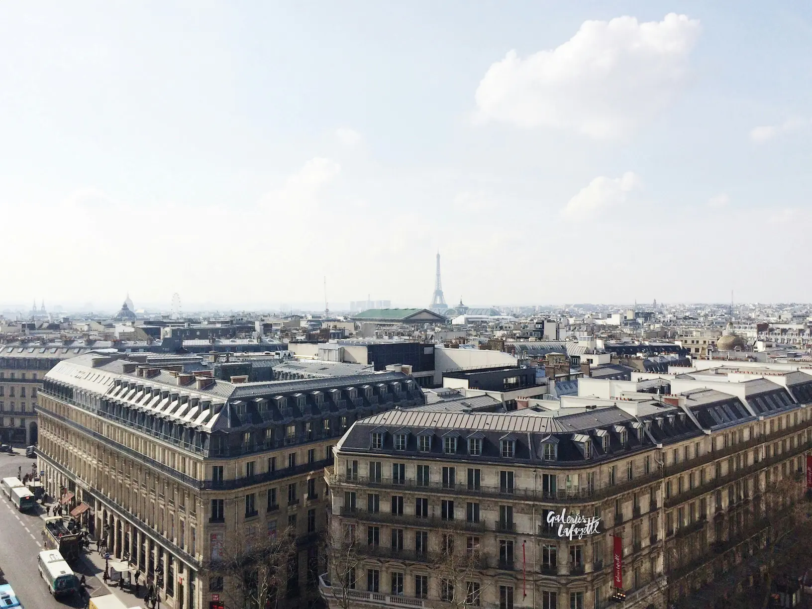 Vue aérienne des toits de Paris avec la Tour Eiffel en arrière-plan et un bâtiment des Galeries Lafayette au premier plan.