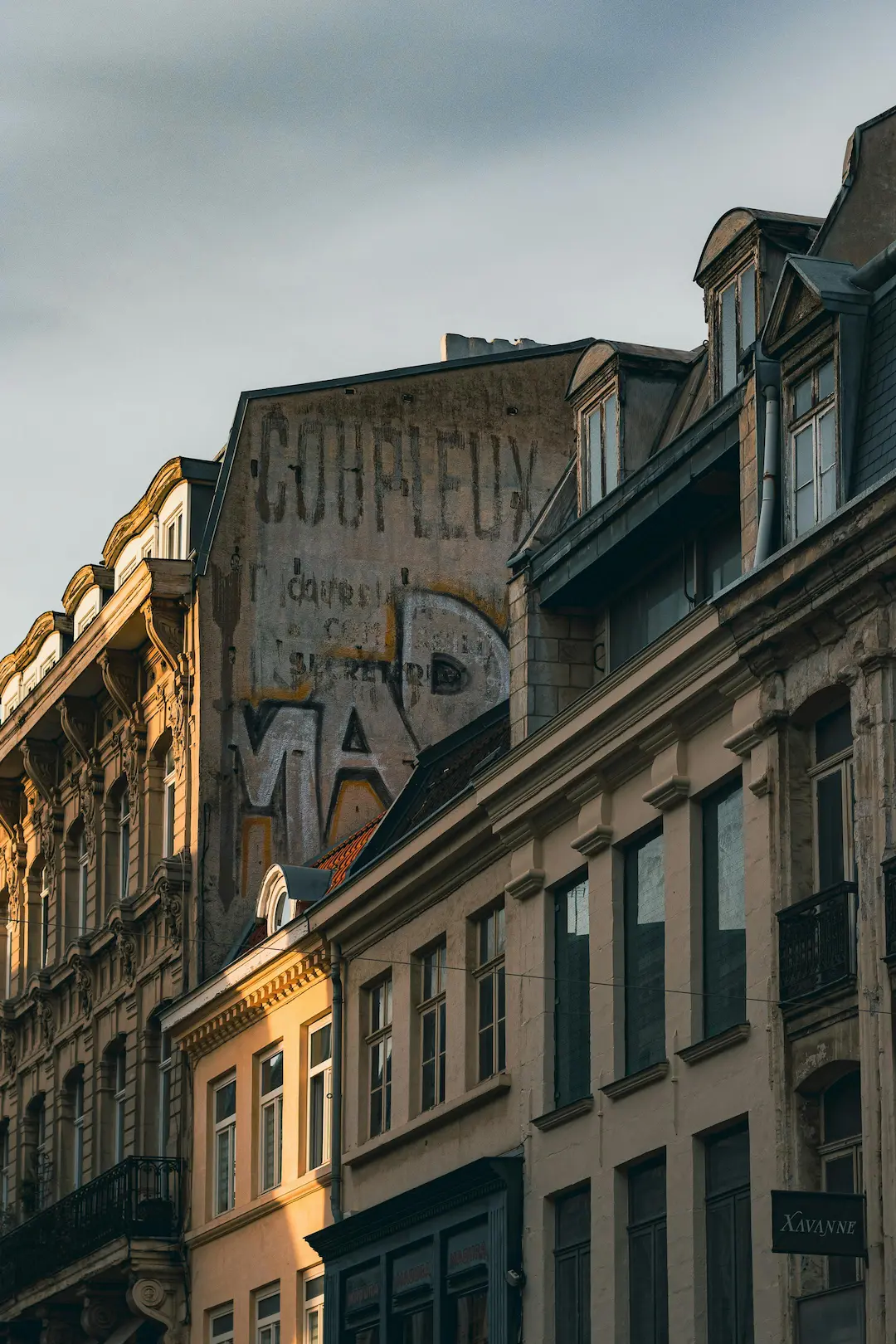 Façades anciennes d'immeubles avec des fenêtres mansardées sous une lumière douce en fin de journée.