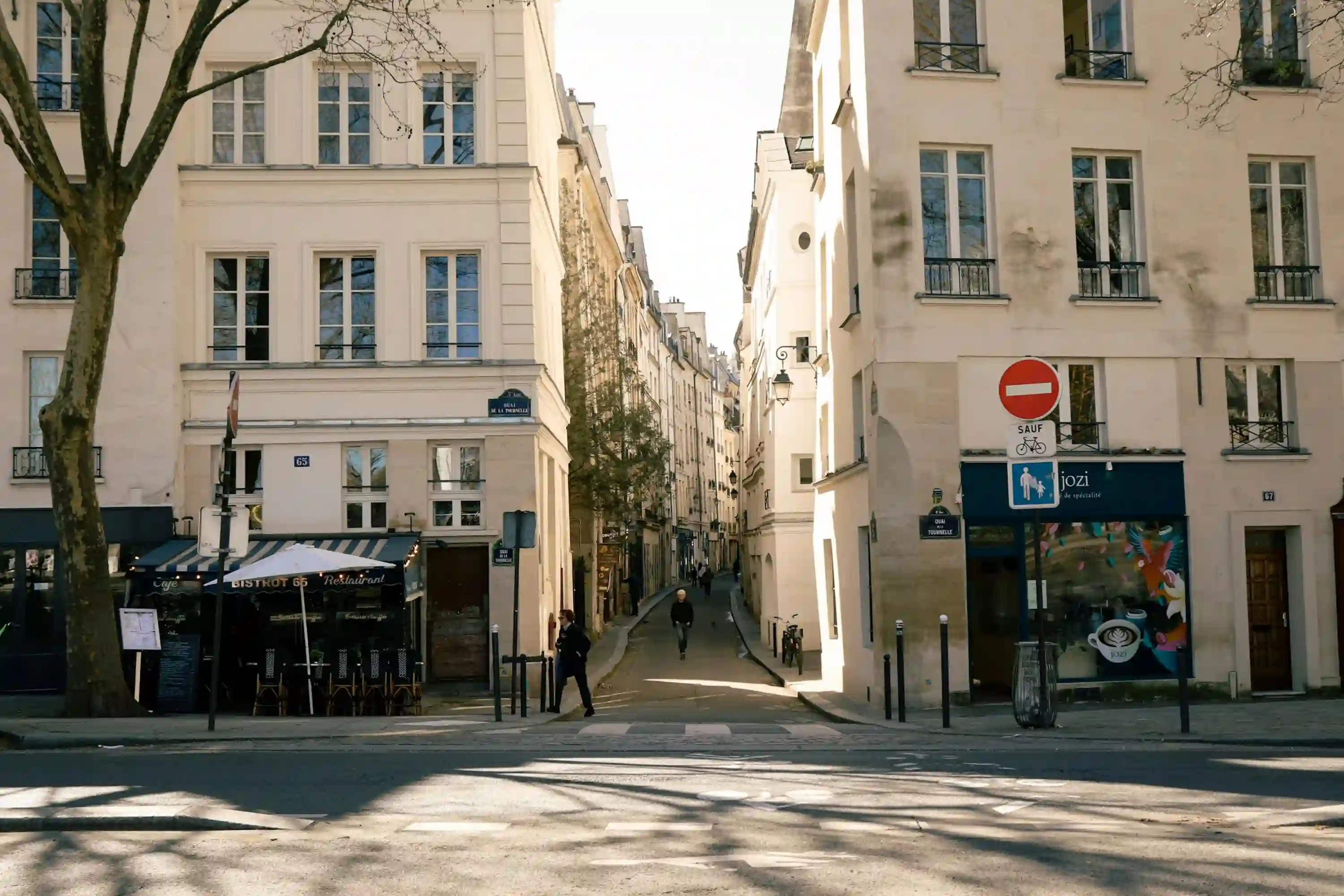 Rue étroite bordée de bâtiments parisiens avec un restaurant Bistrot 65 à gauche et un café Jozi à droite, sous un ciel clair.