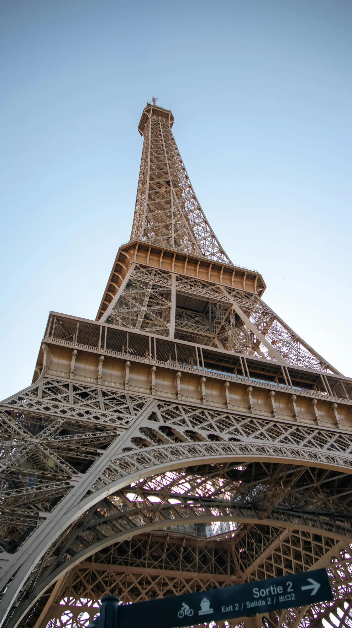 Vue en contre-plongée de la Tour Eiffel avec un panneau indiquant la sortie 2.