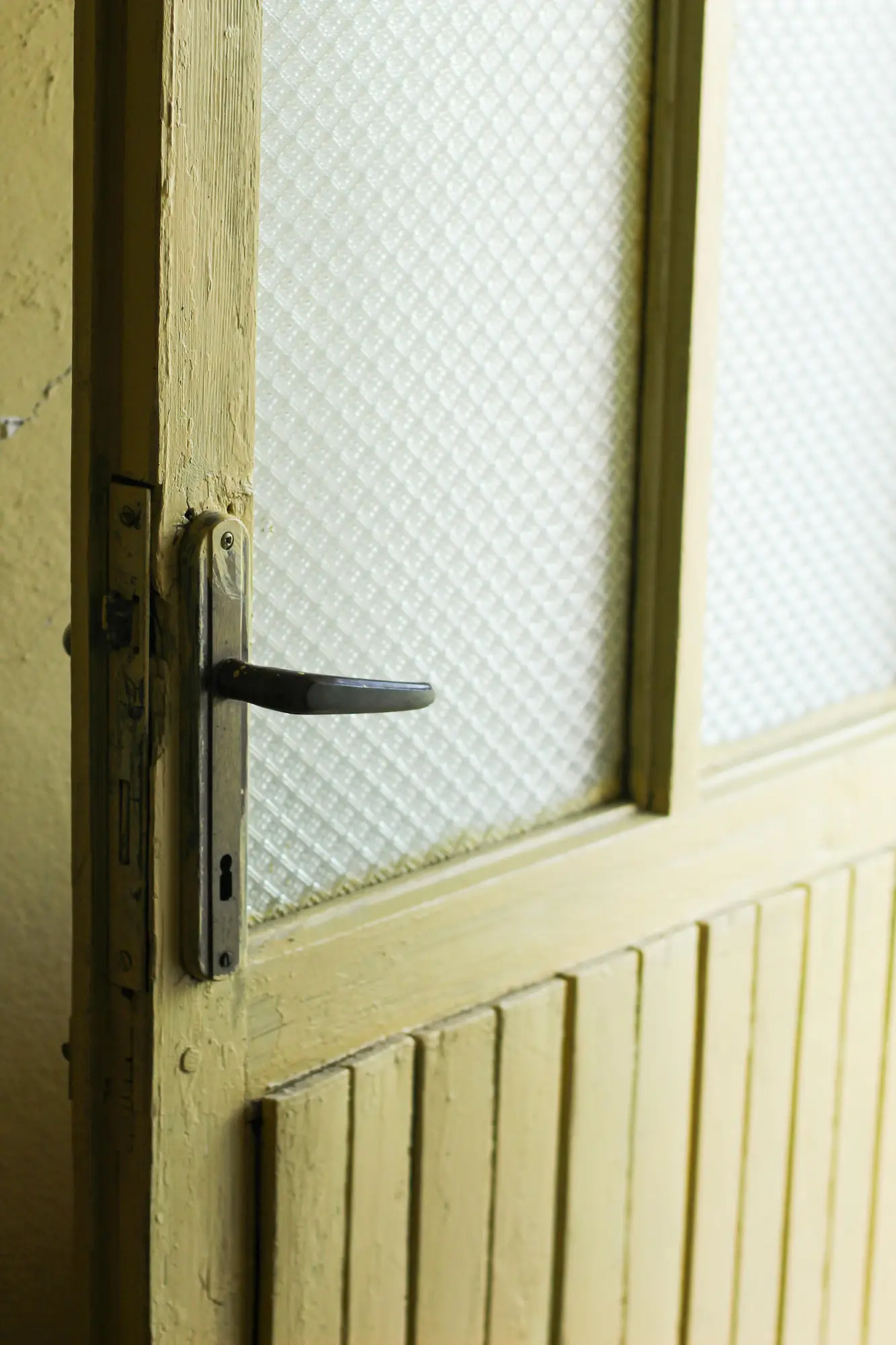 Porte en bois beige avec panneau en verre texturé et poignée métallique noire.