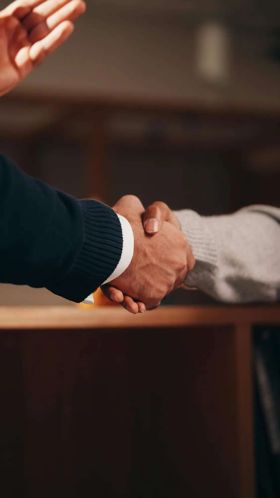 Deux personnes se serrant la main au-dessus d'une surface en bois, signe d'accord ou de salutation.